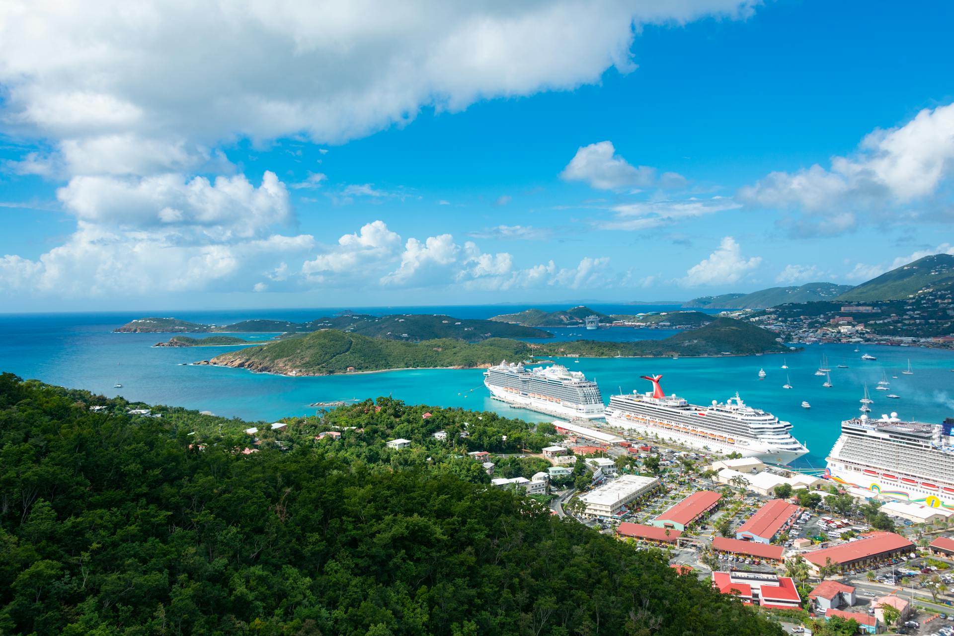 Stunning aerial capture of cruise ships docking in a turquoise harbor surrounded by lush green islands.