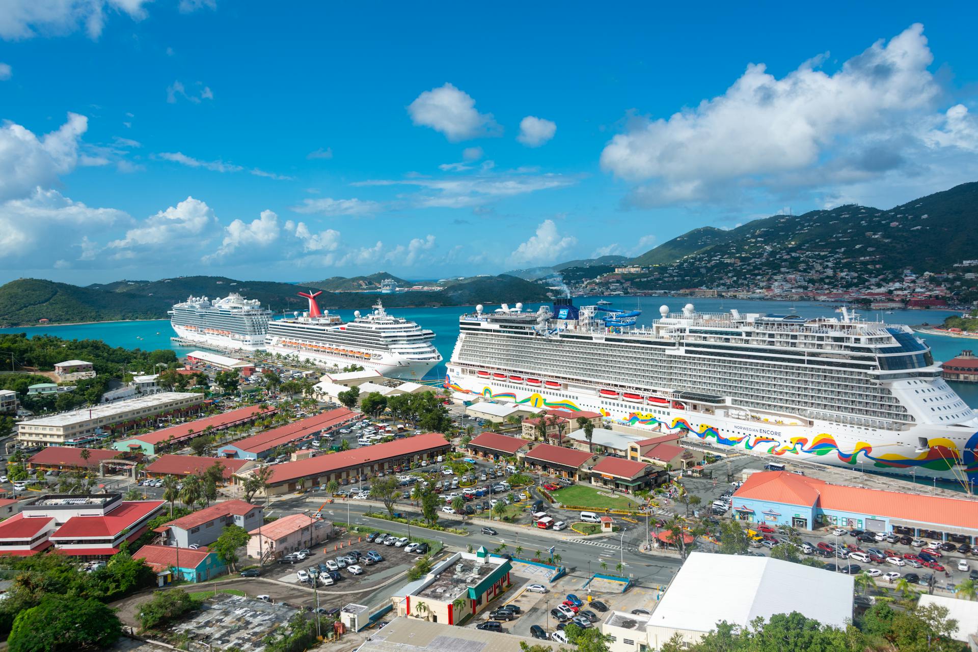 Stunning aerial view of luxurious cruise ships docked in a scenic harbor with hills and clear skies.