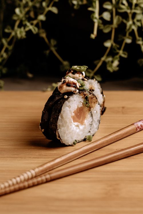 Free Mouth-watering salmon sushi roll with chopsticks on bamboo mat, perfect for food photography. Stock Photo