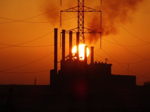 Free A dramatic silhouette of a power plant with smoke stacks and power lines against a golden sunset. Stock Photo