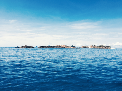 Free A tranquil ocean scene with a rocky island beneath a vast blue sky, ideal for nature themes. Stock Photo