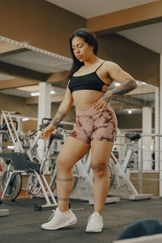 Strong woman with tattoos in gym attire standing confidently indoors.