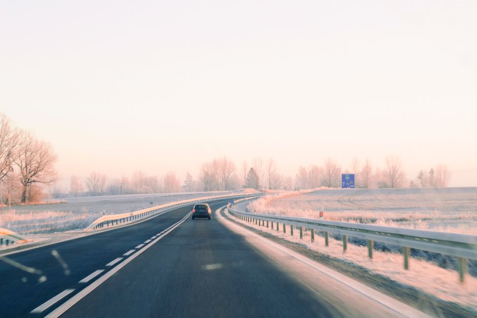 A serene winter drive on a frosty rural road with light snow cover and bare trees.