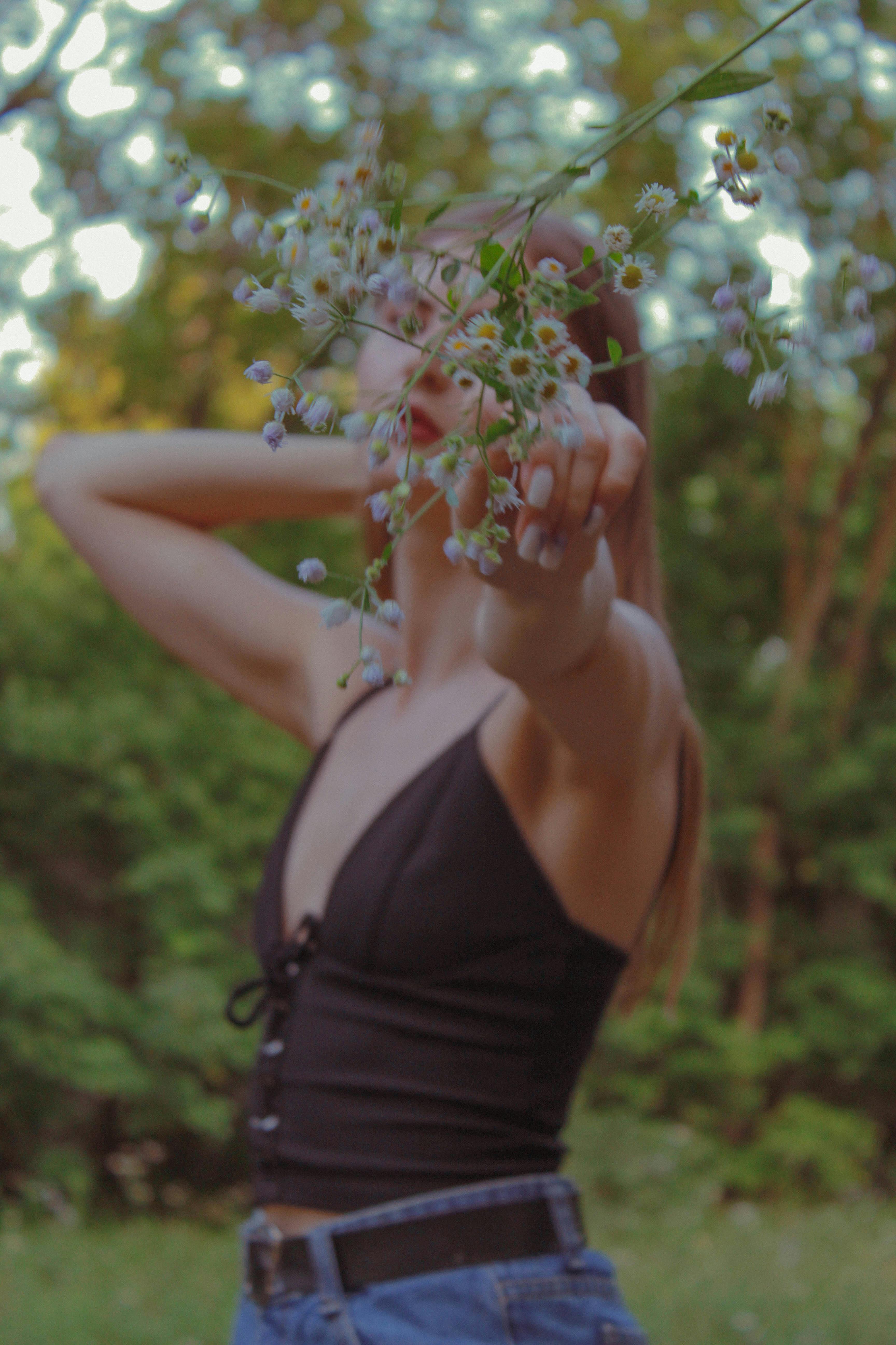 A woman posing with flowers in a lush outdoor setting, embodying a natural and serene vibe.