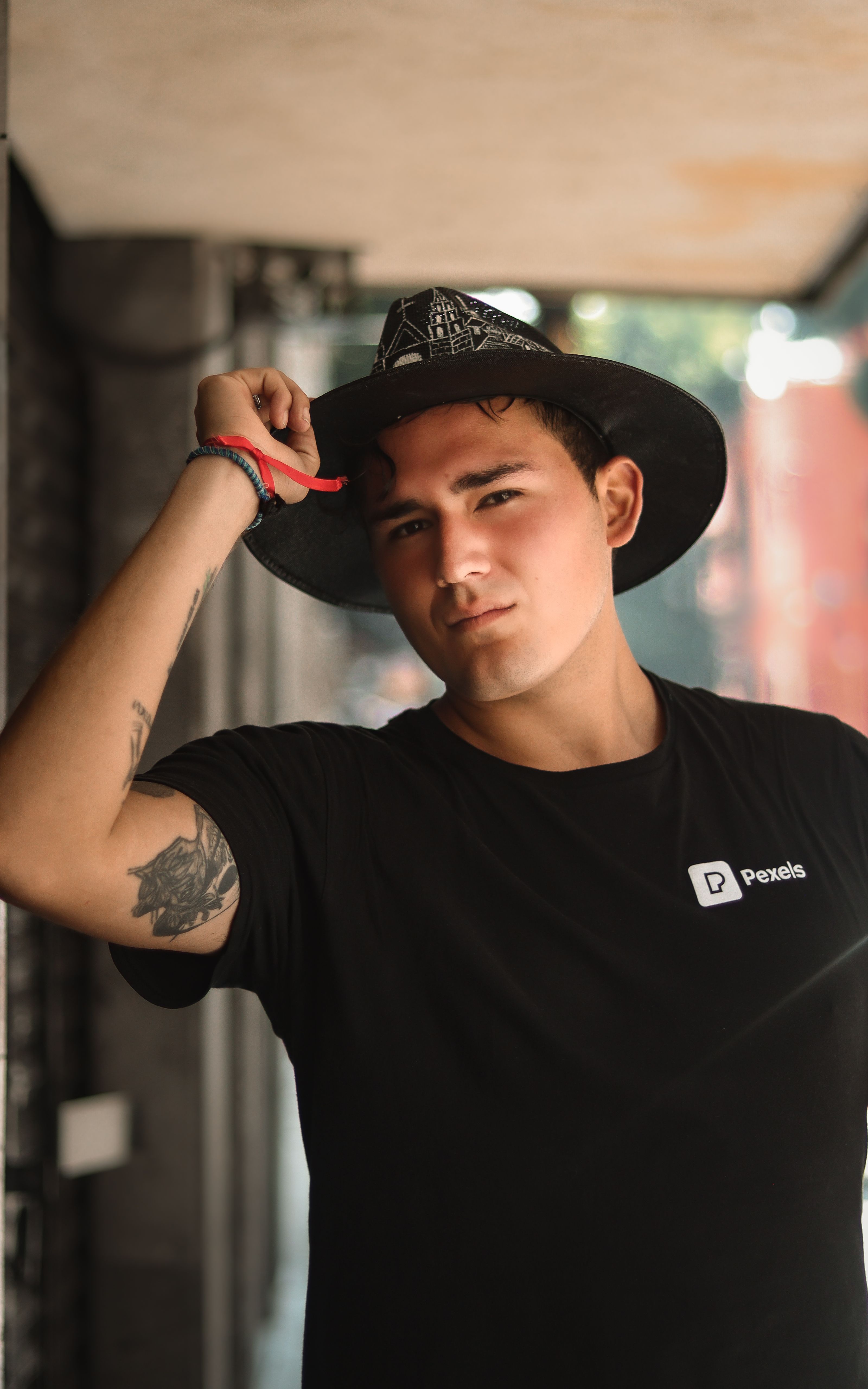 Jovem com tatuagens usando um chapéu, posando em ambiente interno. Fotografia de moda casual.