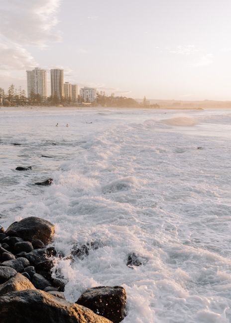 Waves crash on the rocky shore as skyscrapers rise in the Gold Coast, Australia.