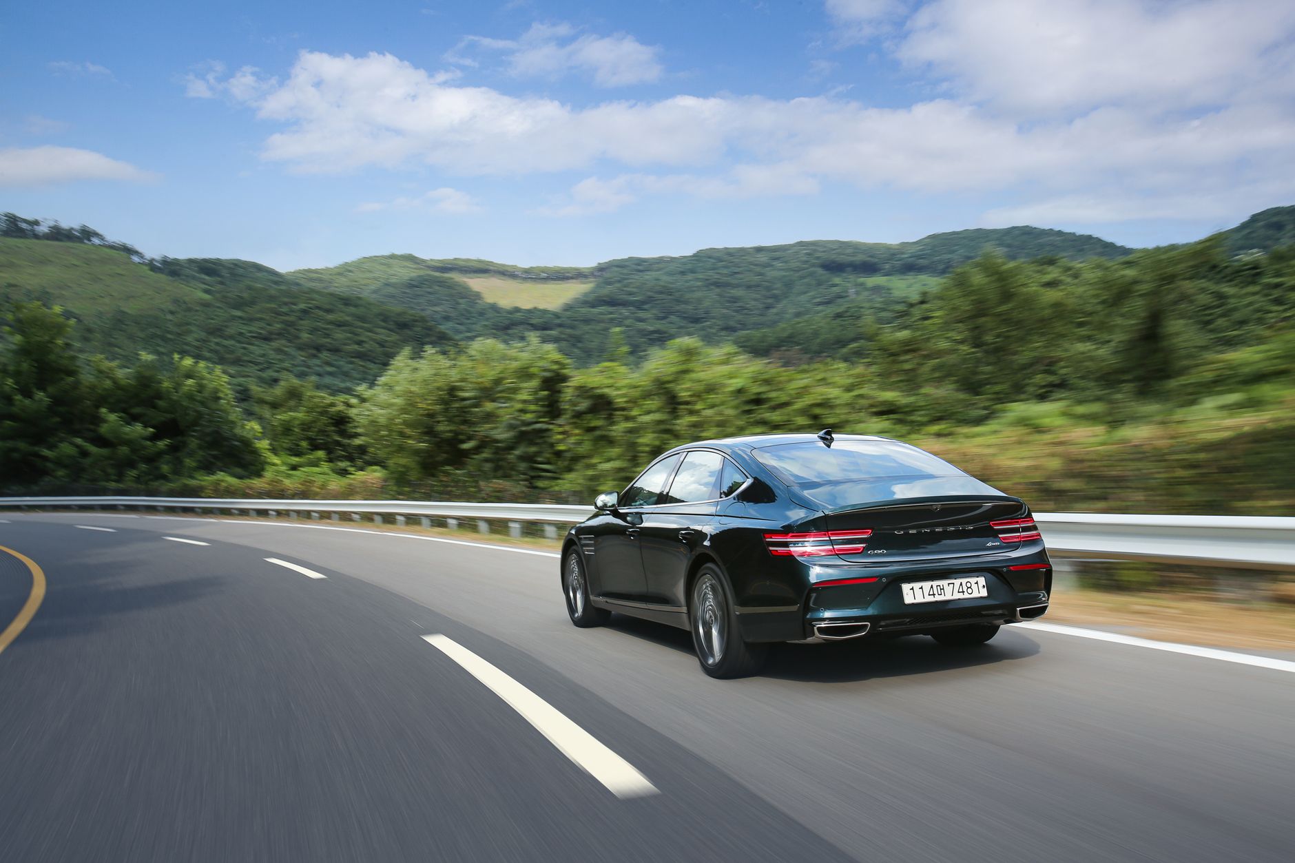 A sleek black Genesis G80 Sport drives on a winding road with verdant mountains in the background.