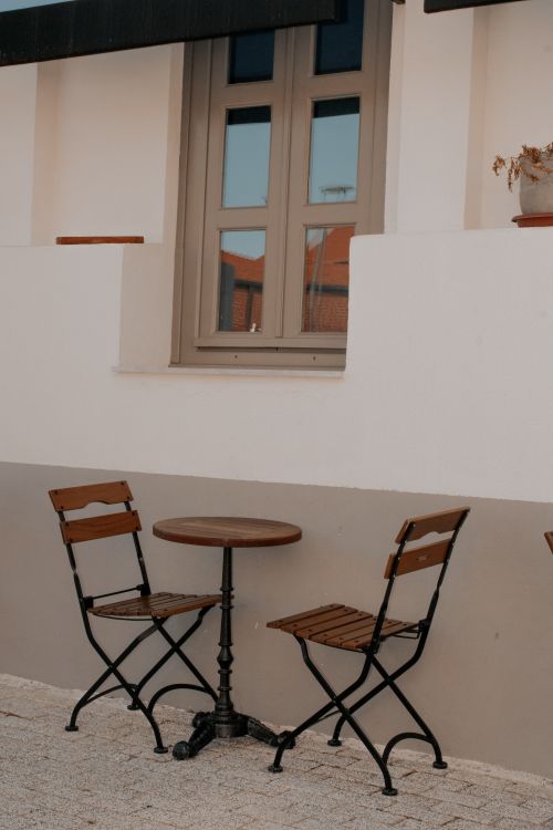 Free Cozy outdoor café scene with wooden chairs and table by a white wall, suggesting a peaceful ambiance. Stock Photo