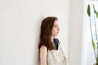 在明亮的室内，一位年轻女子靠在墙上