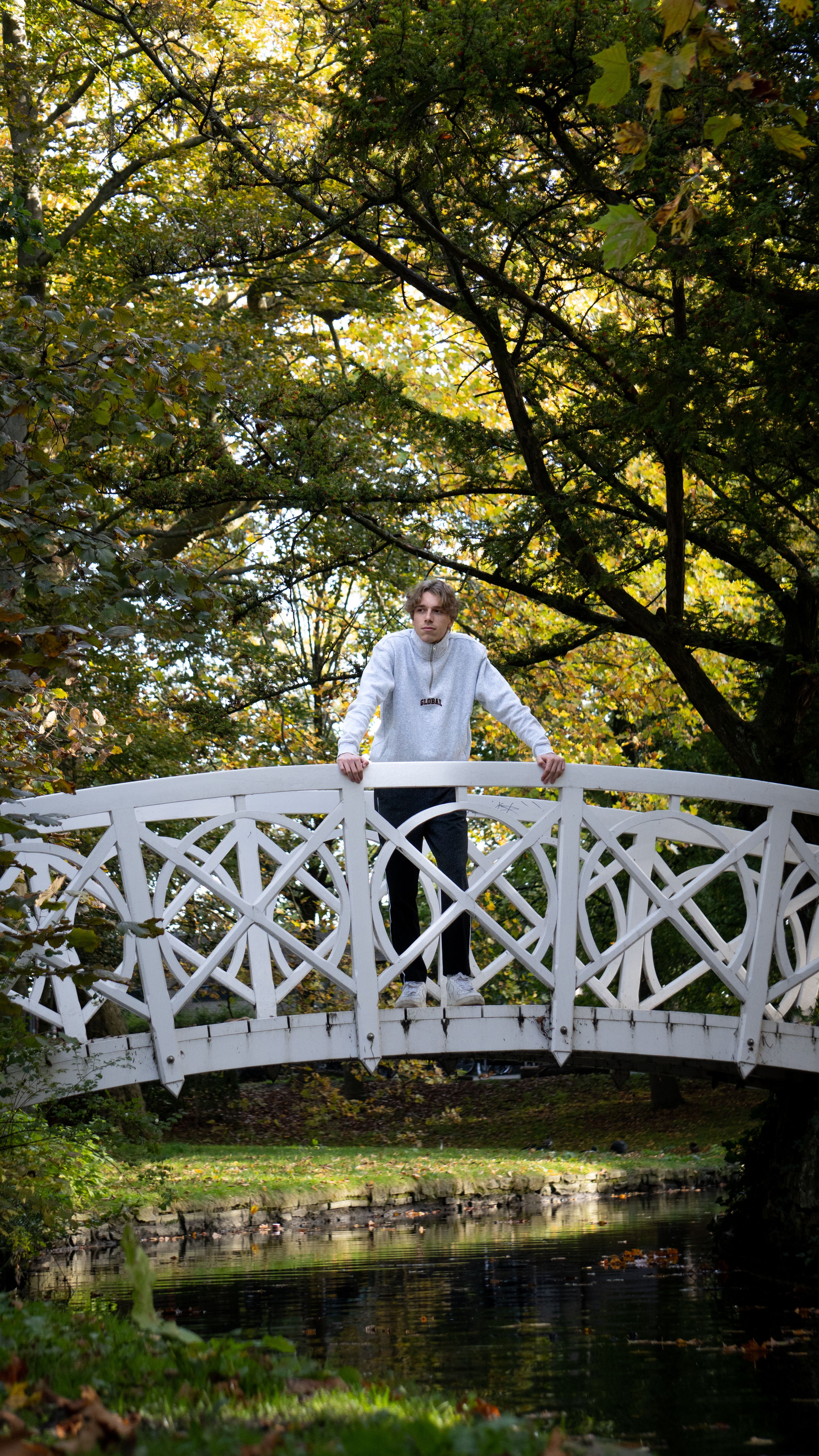 A person enjoying a serene moment on a white footbridge surrounded by autumn foliage.