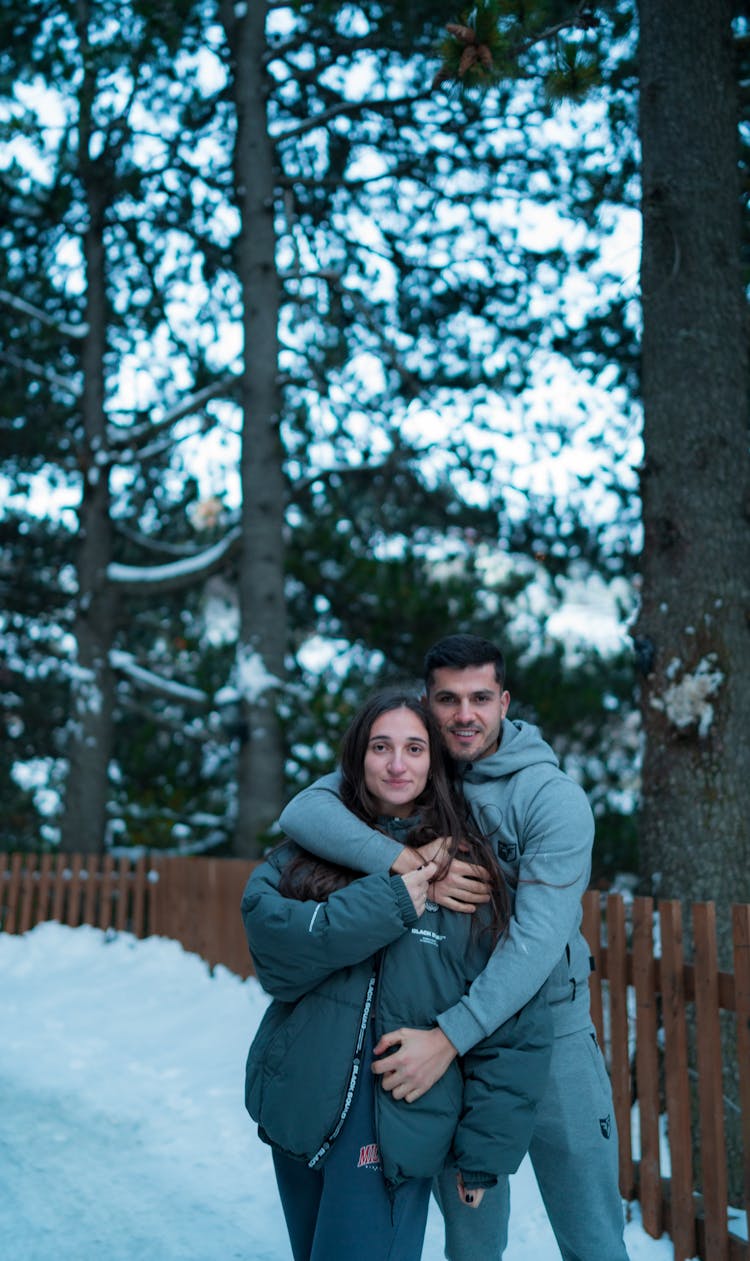 A Couple In Winter Clothes Embracing While Standing Together On A Snow Covered Ground