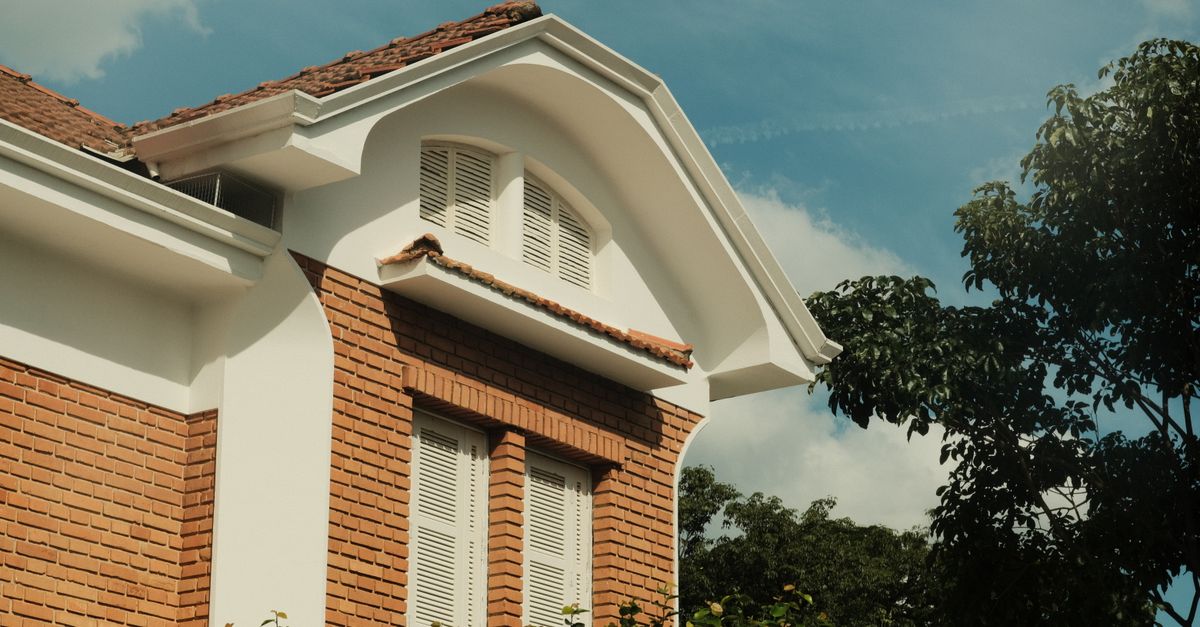 Exterior shot of a brick house featuring an arched roof and white shutters, set against a blue sky.