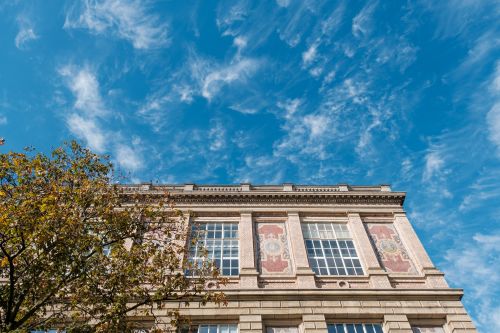 Free Ornate building facade against a bright blue sky with wispy clouds and tree. Stock Photo