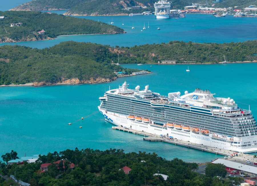 Aerial view of a luxury cruise ship docked in a turquoise Caribbean harbor on a sunny day.