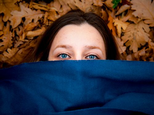 Free Close-up of a woman's blue eyes peeking from behind a blue cloth in autumn leaves. Stock Photo