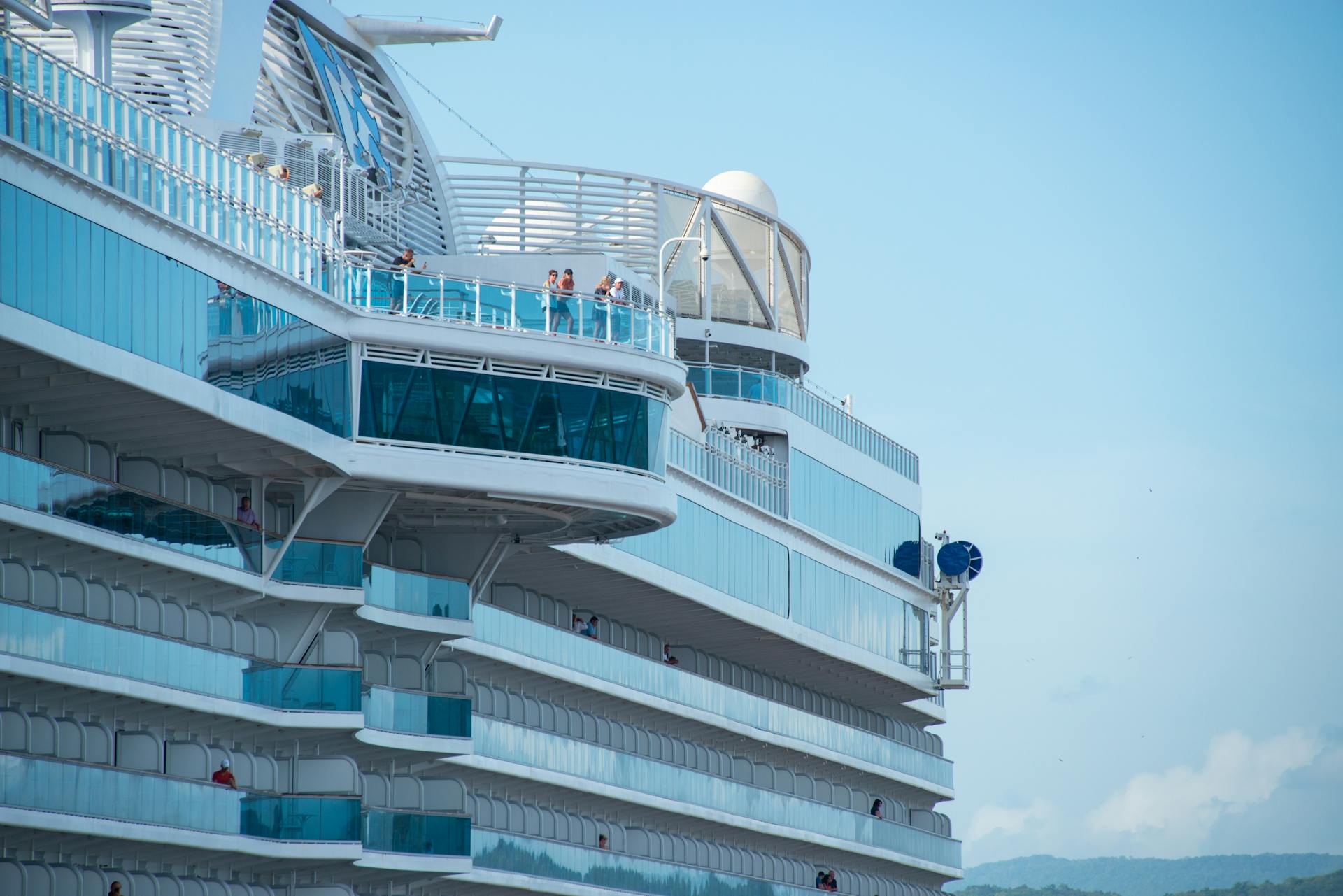 Close-up view of a modern cruise ship with people on deck, under a clear blue sky.