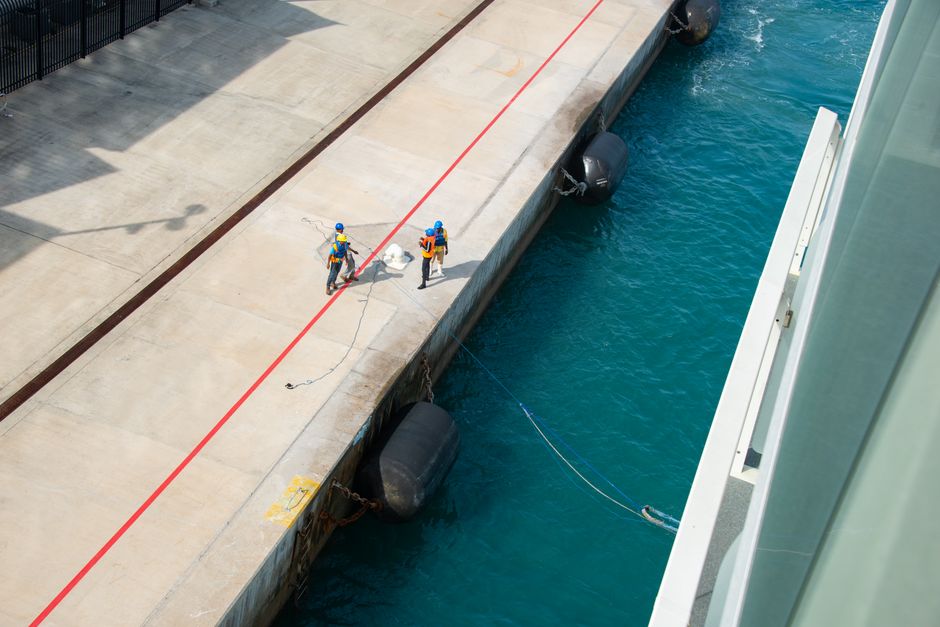 High angle view of workers preparing a vessel for docking at a sunlit pier.