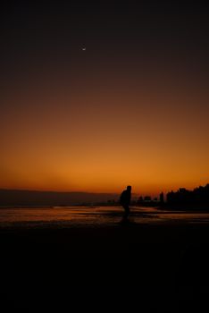 A silhouette strolls along the shore during a dramatic sunset, creating a tranquil evening scene.