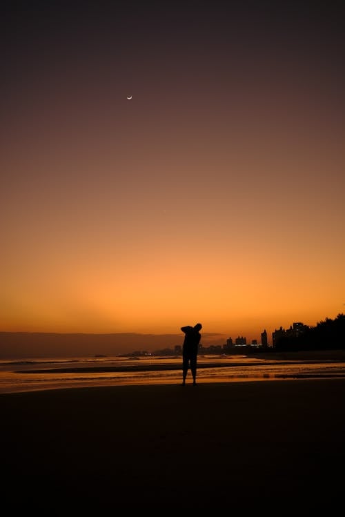 Person Standing on Shore During Sunset