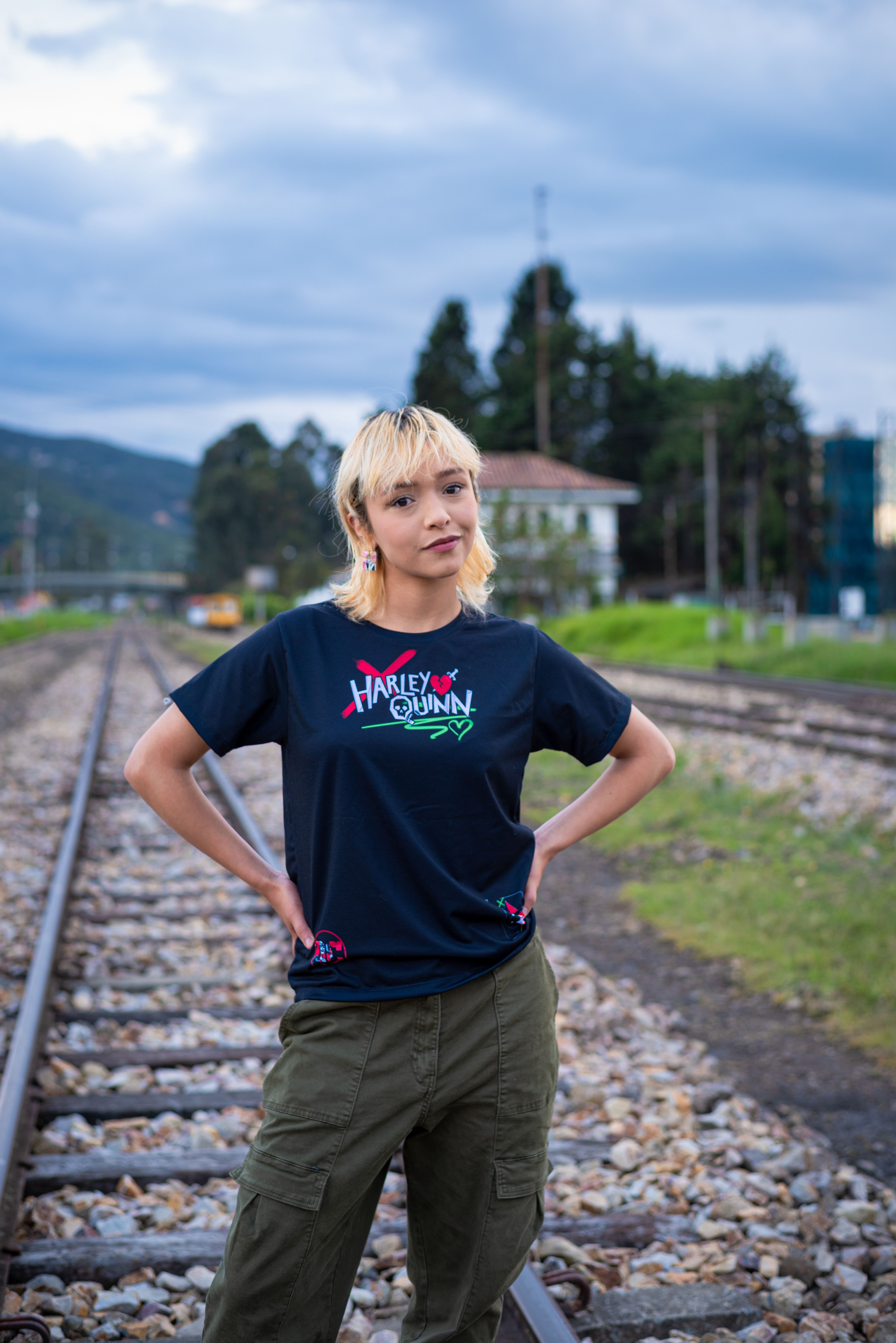 Woman in streetwear posing confidently on railway tracks outdoors.