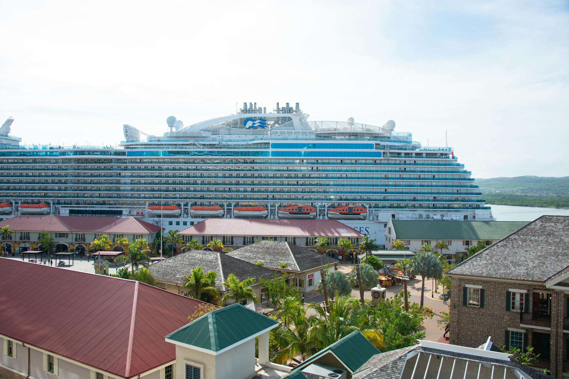 Luxurious cruise ship docked in tropical harbor amidst vibrant buildings.
