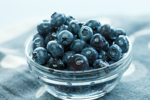 Free Close-up of fresh ripe blueberries in a clear glass bowl on a soft textured background. Stock Photo