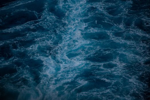 Aerial shot of ocean waves with a moody, dark blue tone, capturing turbulent sea patterns.
