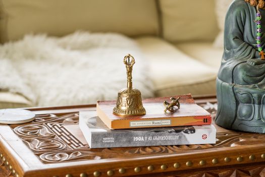 Close-up of a decorative bell and books on a carved wooden table in a cozy setting.