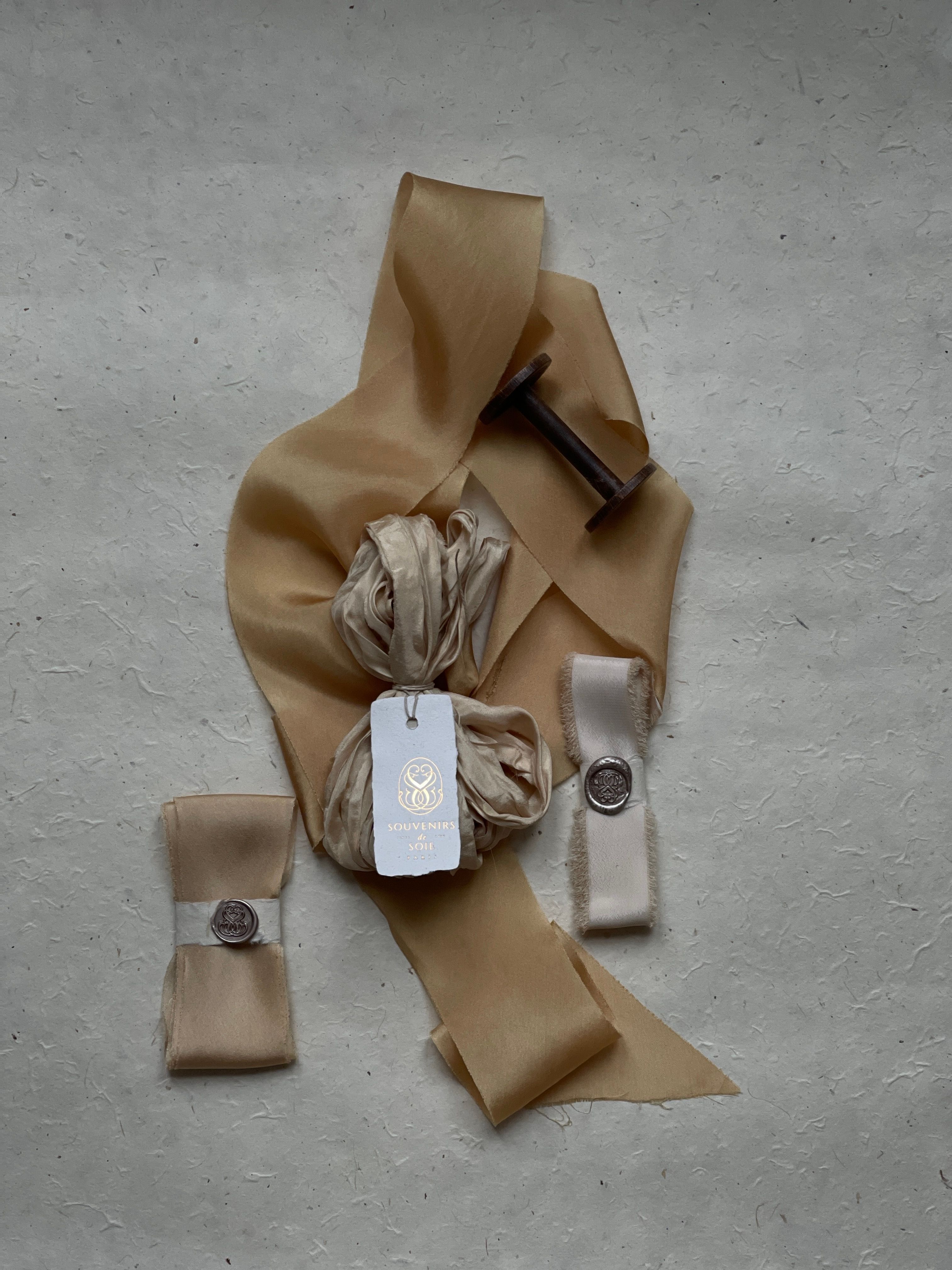 A beautifully arranged flat lay of beige fabric and ribbon on a textured gray background, with vintage elements.
