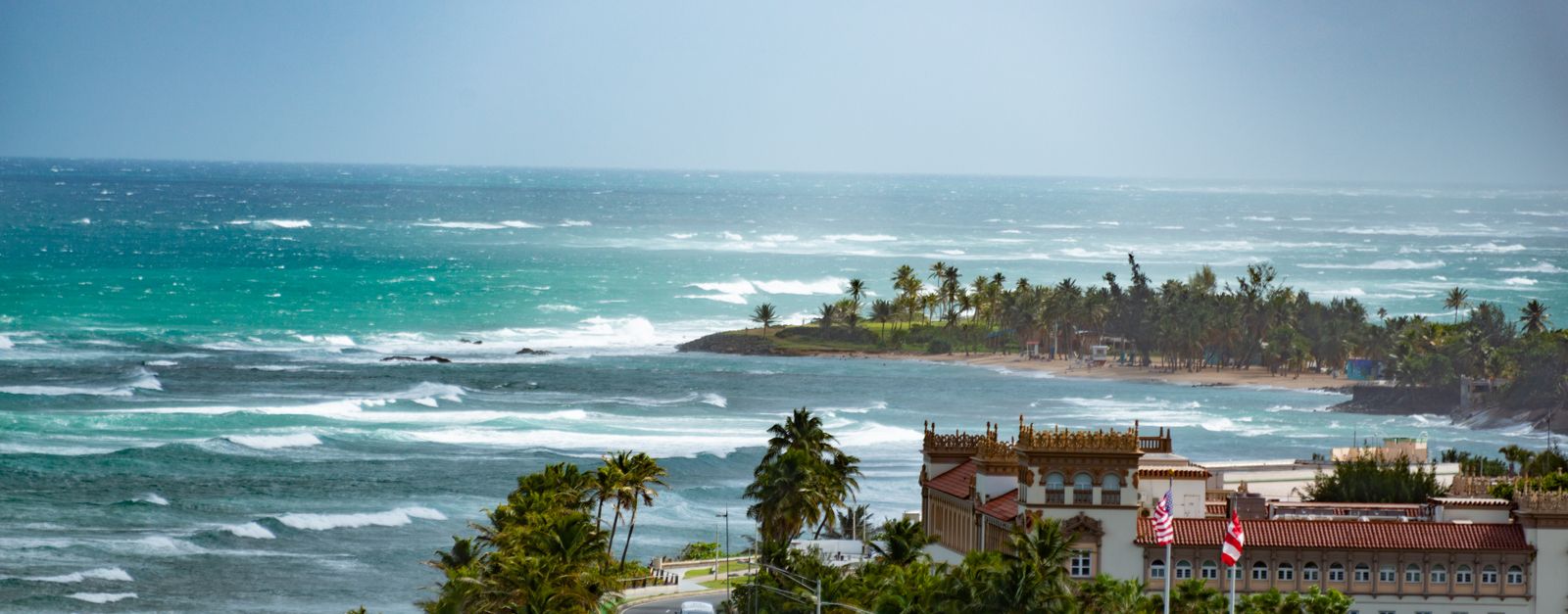 A breathtaking aerial view of a tropical coastline with waves crashing against the shore and lush palm trees.