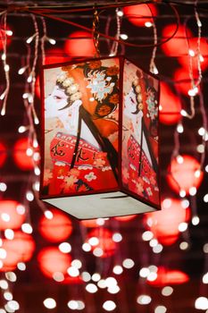 Illuminated traditional Chinese lantern with bokeh red lights.