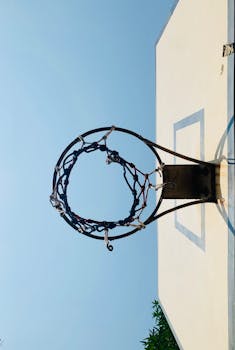 A sunlit basketball hoop from below against a clear sky in Dhaka.