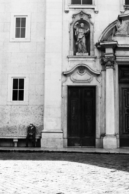 Black and white photo of a man sitting by a historic doorway in Lisbon, Portugal.
