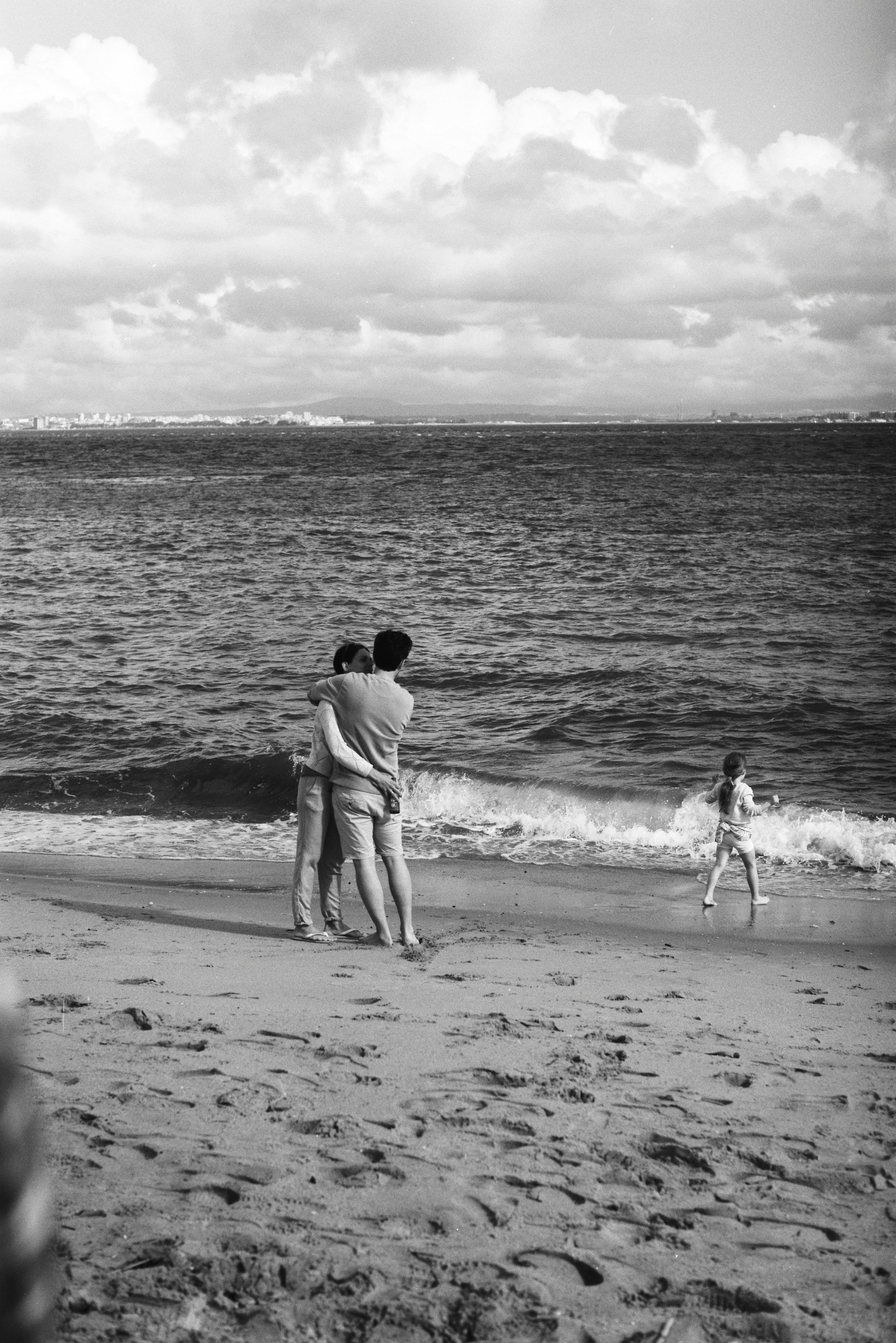 Black and white photo of a family embracing on a scenic Lisbon beach.