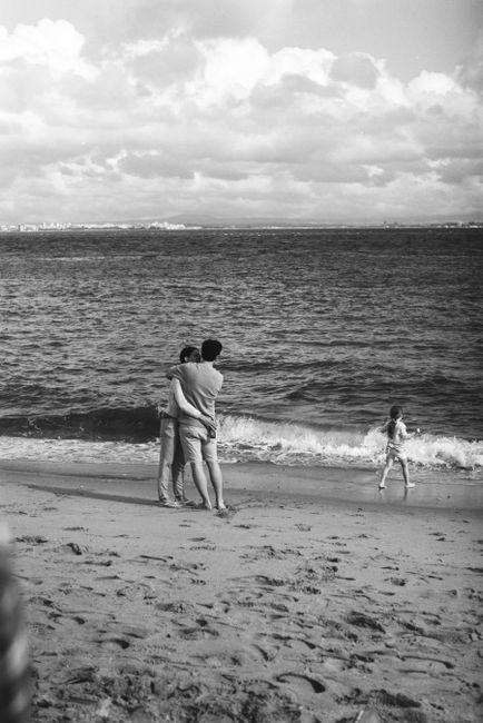 Black and white photo of a family embracing on a scenic Lisbon beach.