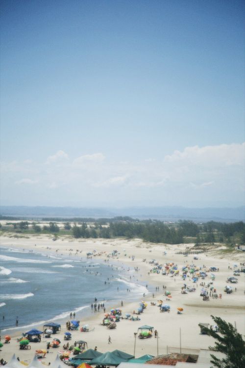 Free Aerial view of a busy beach with tourists and colorful umbrellas under a clear blue sky. Stock Photo