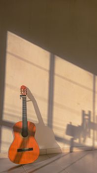 An acoustic guitar leaning against a sunlit wall, casting artistic shadows indoors.