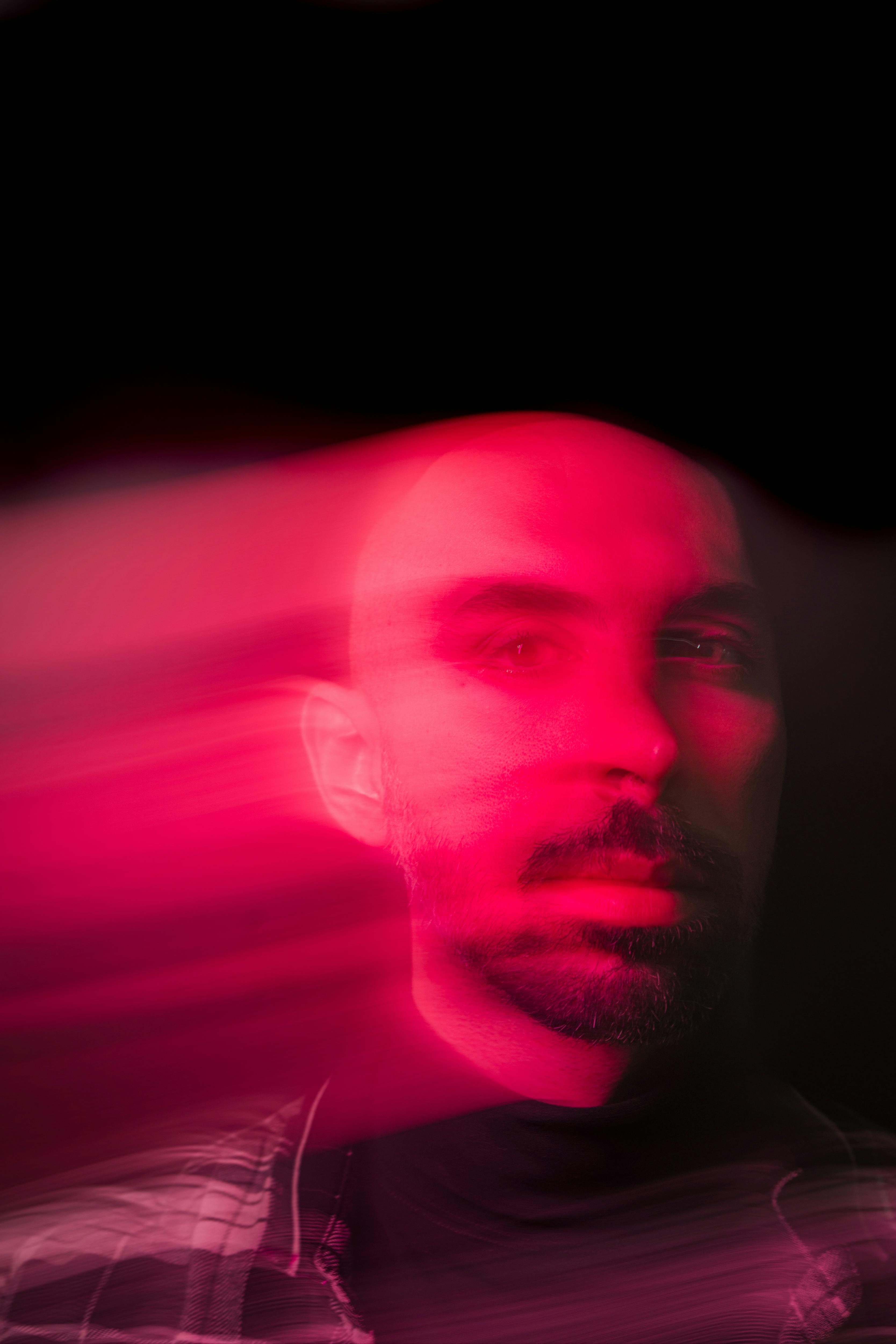 Blurred portrait of a bearded man with artistic pink light trails creating a dramatic effect.