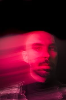 Blurred portrait of a bearded man with artistic pink light trails creating a dramatic effect.