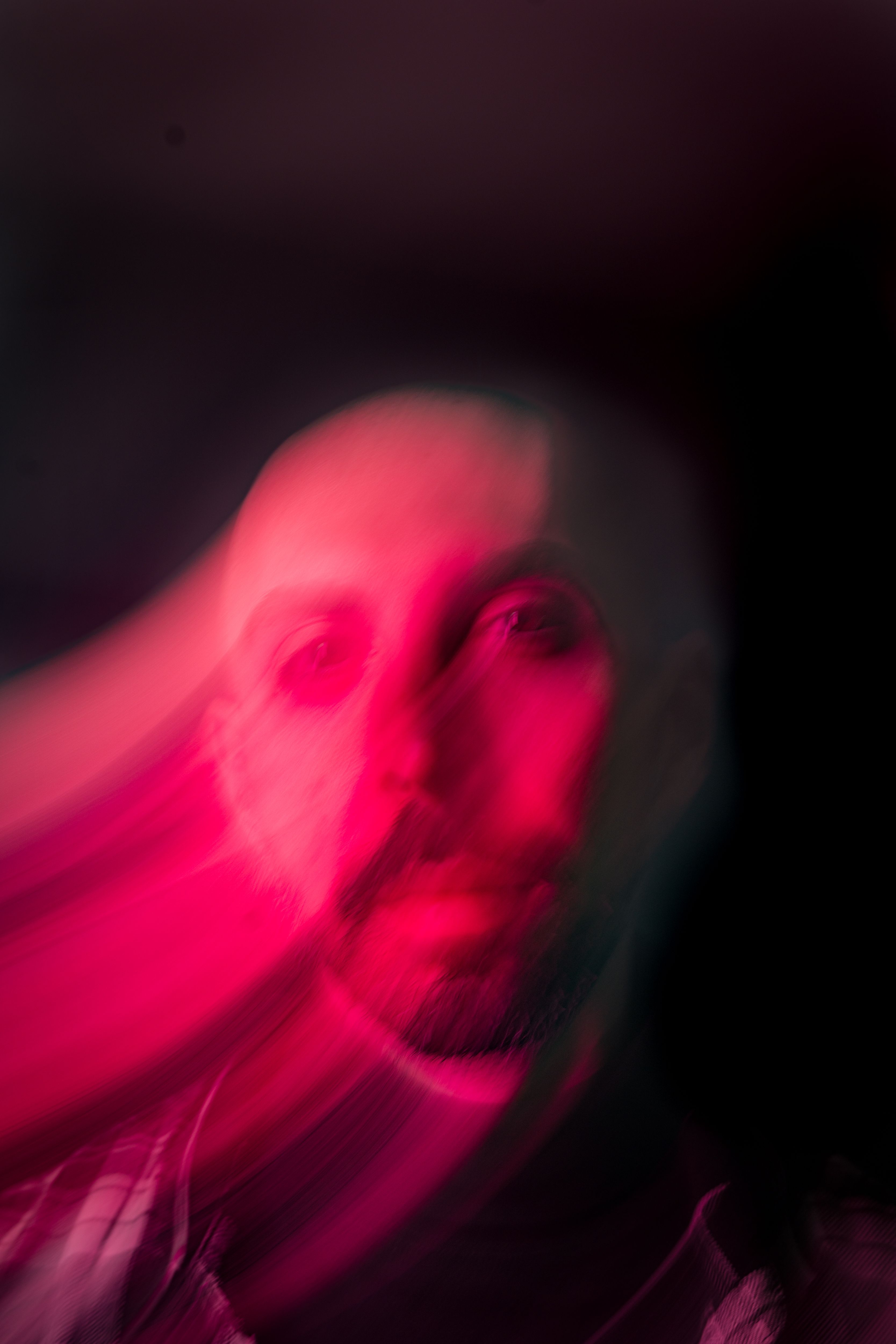 Blurry abstract portrait with pink light and motion blur, creating a surreal effect.
