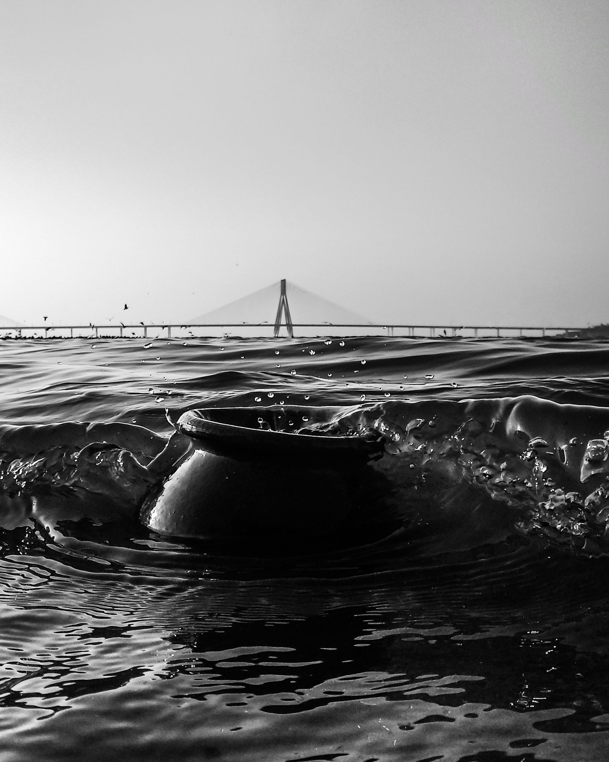 A monochrome view of Bandra-Worli Sea Link with ocean waves and a submerged vase in Mumbai, India.