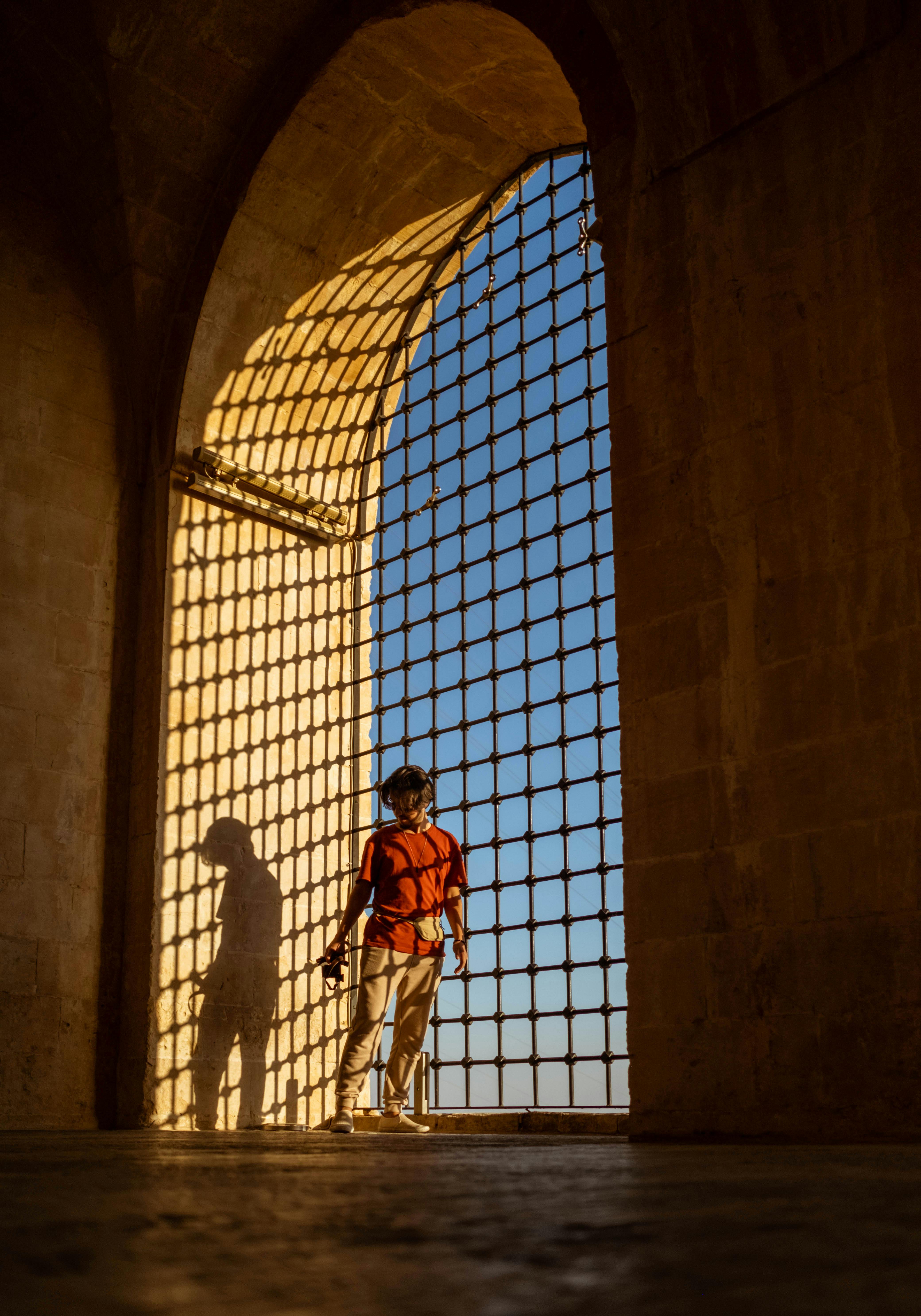A man stands in an ancient archway in Mardin, casting a shadow at sunset.