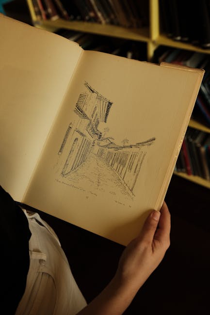 A person's hands holding an open book with a drawing, set against a bookshelf background.