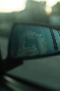 Reflection of a photographer taking a picture through a car side mirror during the day.