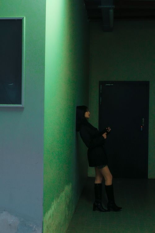 Free Silhouetted woman leans against a green-lit wall, creating a moody atmosphere. Stock Photo