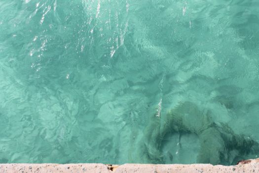 Top view of clear turquoise water by the shoreline, showing ripples and reflections.