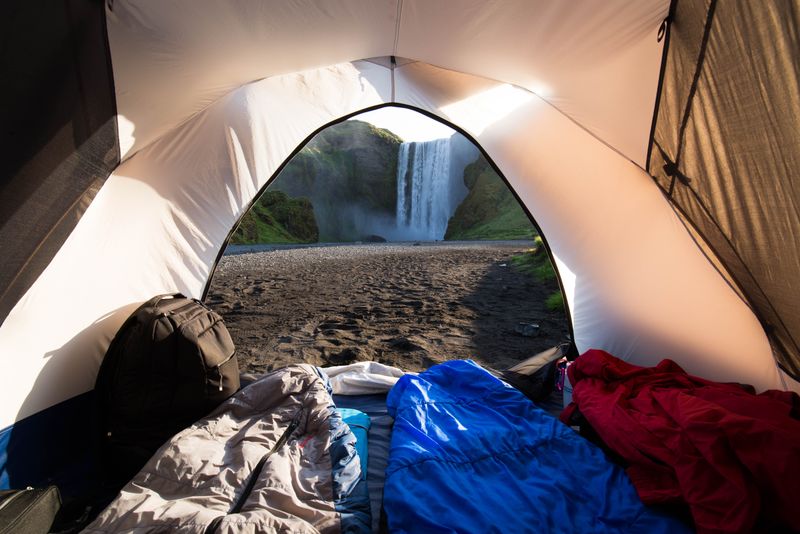 Quilts laid out inside a tent looking toward a waterfall — photo by Andrew Main Oster on Pexels