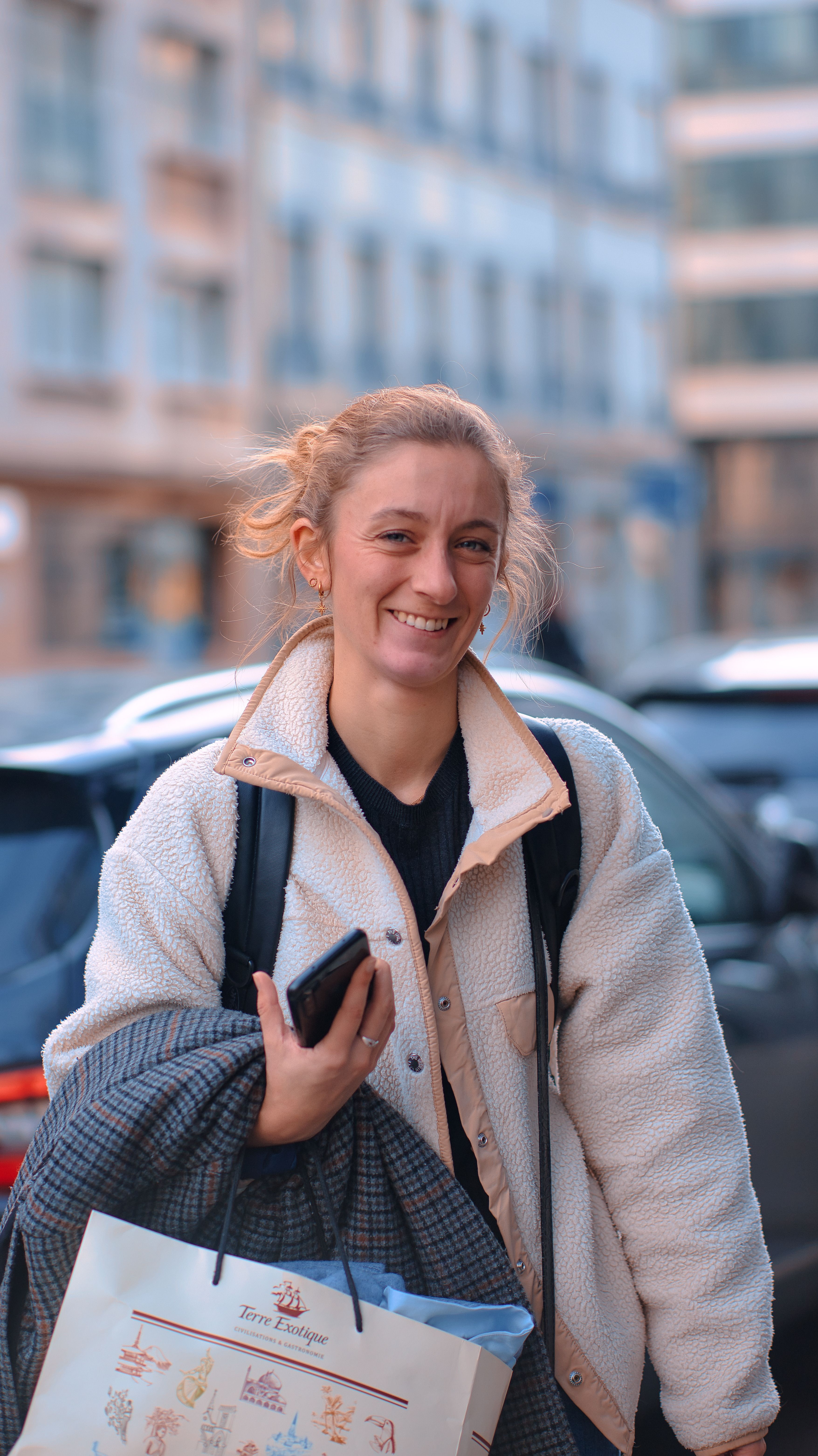Smiling woman holding a shopping bag on a bustling city street, embodying urban lifestyle.