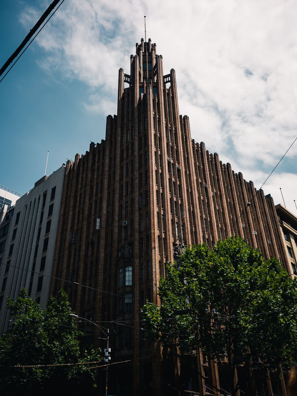 A magnificent Art Deco skyscraper under a clear blue sky with lush trees at its base.. pexels, magnificent, deco