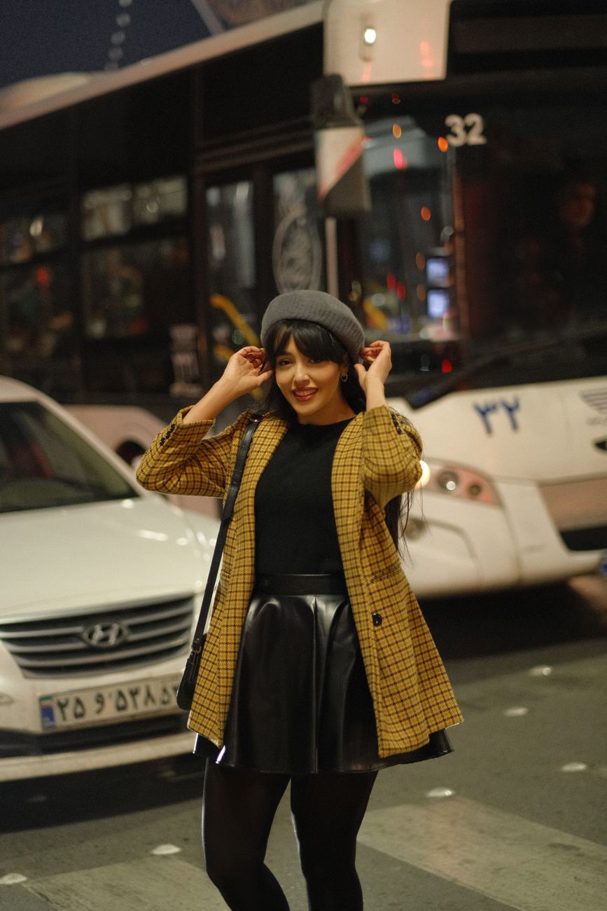 Stylish woman wearing a beret and yellow jacket posing confidently on a city street at night.